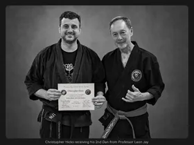 Christopher Hicks standing beside Grandmaster Leon Jay, holding his 2nd Dan certificate